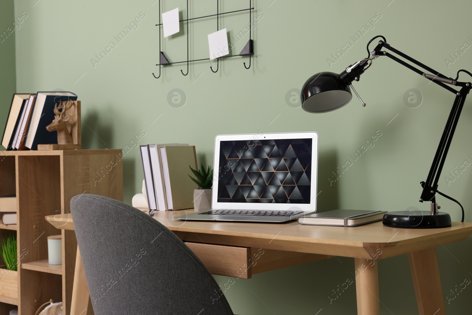 Photo of Modern laptop, books, lamp and stationery on wooden desk near green wall. Home office