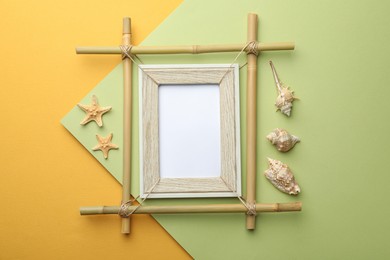 Photo of Empty bamboo frame, starfishes and seashells on color background, flat lay