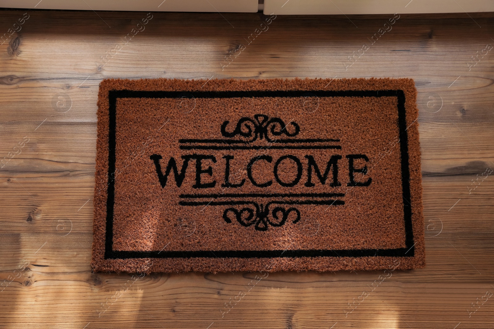 Photo of Door mat with word Welcome on wooden floor, top view