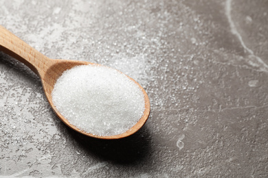 Spoon of white sugar on marble table, closeup. Space for text