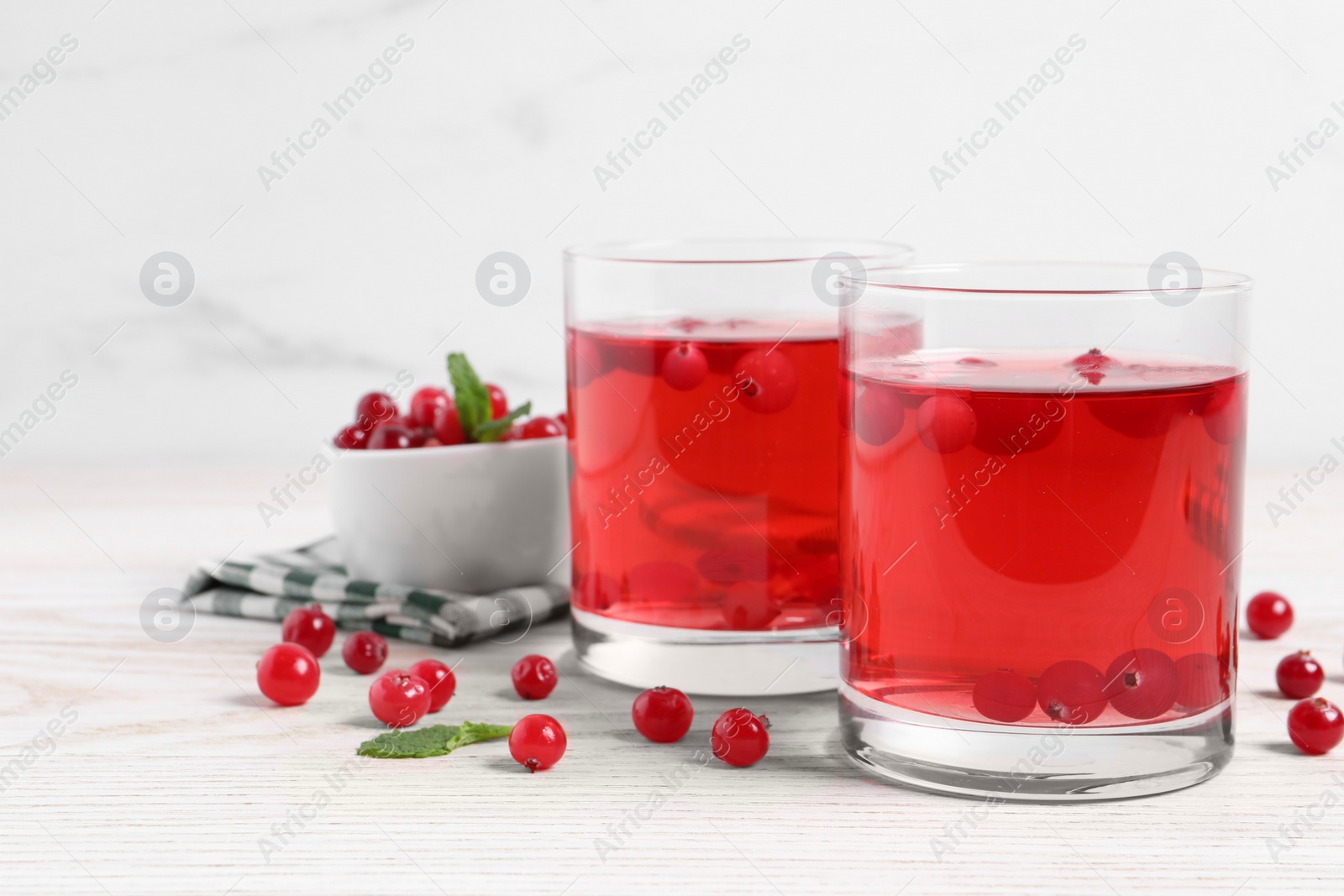 Photo of Tasty cranberry juice in glasses and fresh berries on white wooden table. Space for text