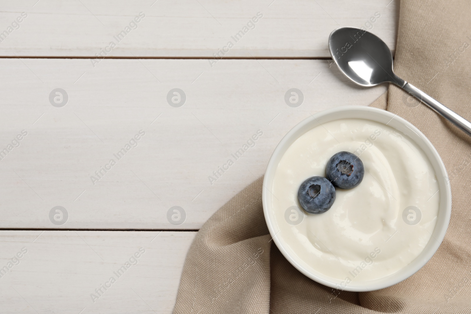 Photo of Bowl of yogurt with blueberries served on white wooden table, flat lay. Space for text