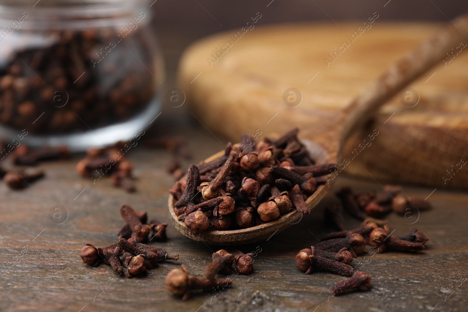 Photo of Spoon with aromatic cloves on wooden table, closeup