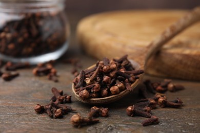 Photo of Spoon with aromatic cloves on wooden table, closeup