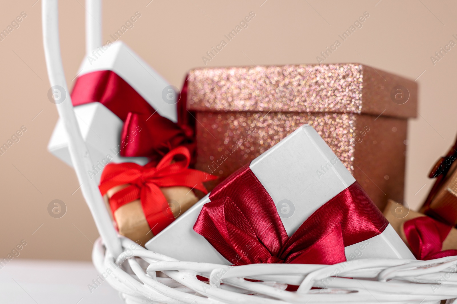Photo of Wicker basket full of gift boxes on white table against beige background