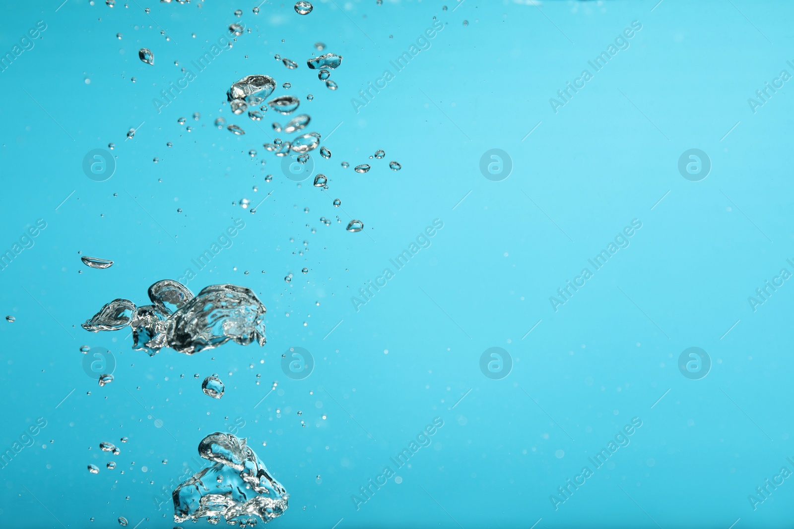 Photo of Air bubbles in water on light blue background. Space for text