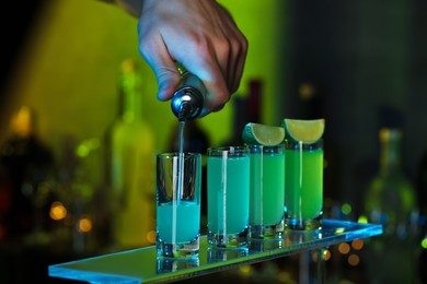 Bartender pouring alcohol drink into shot glass on blurred background, closeup