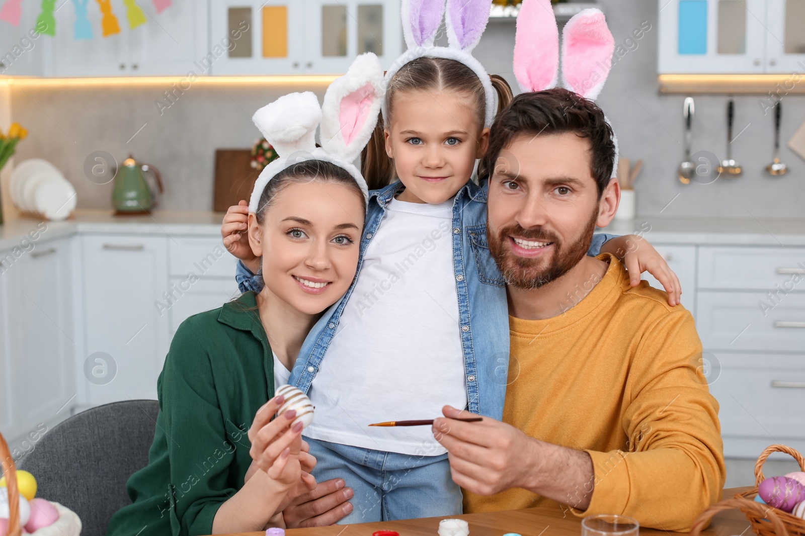 Photo of Happy family with Easter eggs at table in kitchen