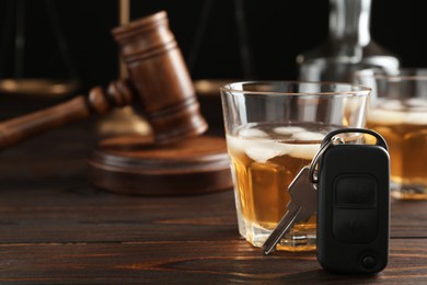 Photo of Car key, glass of alcohol near gavel on wooden table, space for text. Dangerous drinking and driving