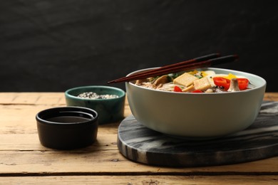 Photo of Noodle soup. Bowl of delicious ramen and chopsticks on wooden table, closeup