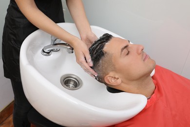 Professional hairdresser washing client's hair at sink in salon, closeup