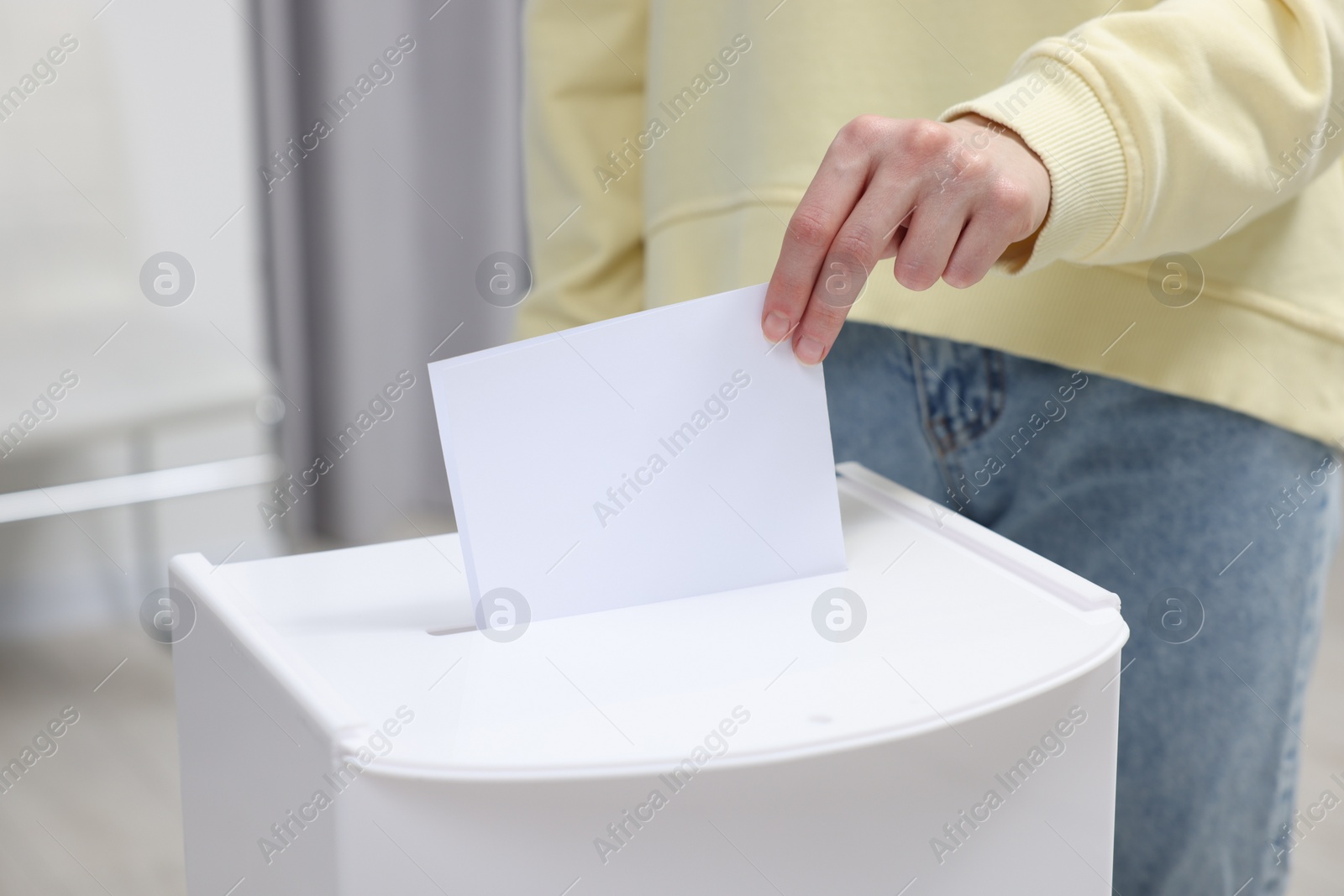 Photo of Woman putting her vote into ballot box on blurred background, closeup