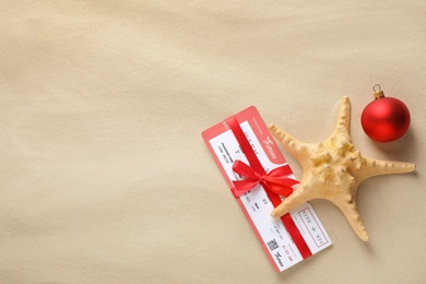 Photo of Airline ticket with red bow, starfish, festive ball and space for text on sand, flat lay. Christmas vacation