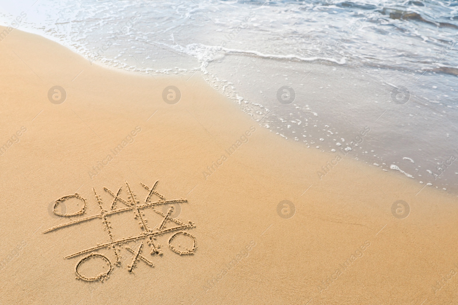 Photo of Tic tac toe game drawn on sand near sea, space for text