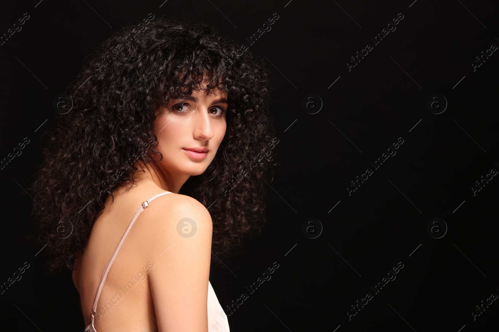 Photo of Beautiful young woman with long curly hair on black background. Space for text