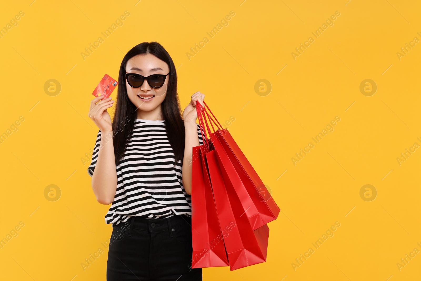 Photo of Happy woman with shopping bags and credit card on yellow background. Space for text