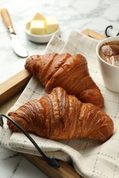 Photo of Tray with tasty croissants served on white marble table, closeup