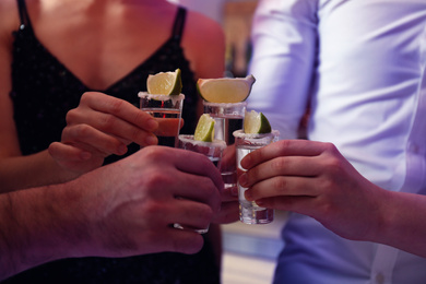 Photo of Young people toasting with Mexican Tequila shots in bar, closeup