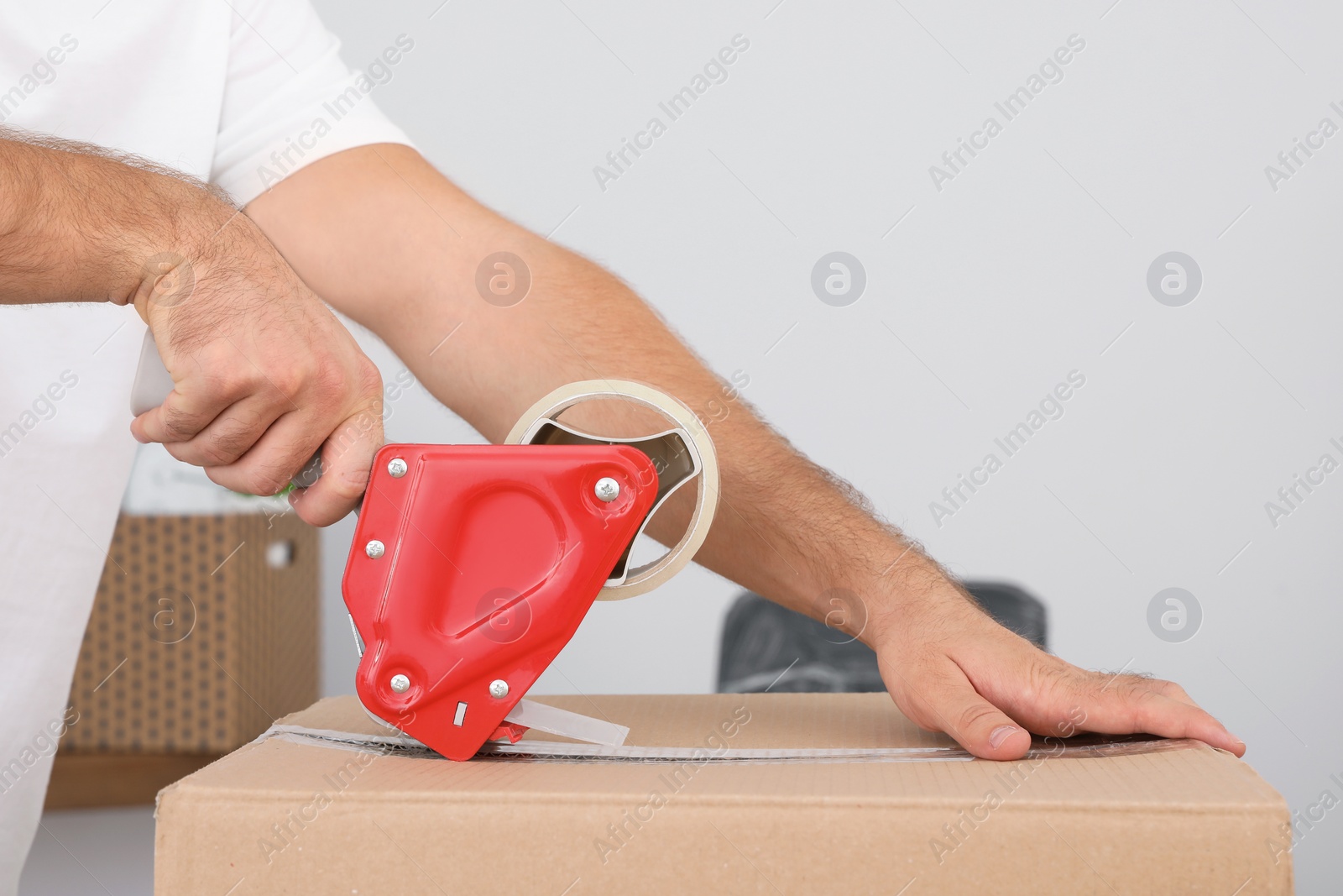 Photo of Young worker packing cardboard box in room, closeup. Moving service