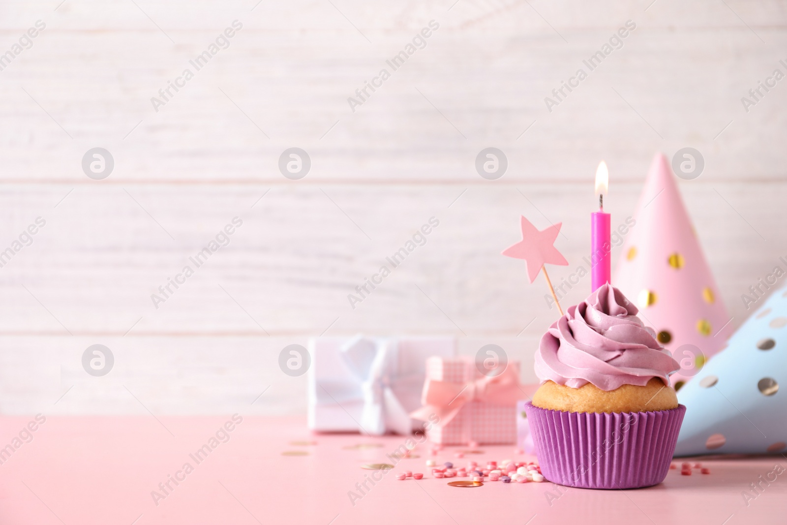 Photo of Birthday cupcake with burning candle, party hats and gift boxes on pink table. Space for text