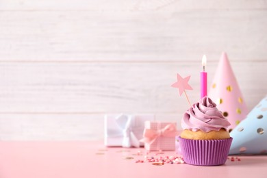 Birthday cupcake with burning candle, party hats and gift boxes on pink table. Space for text