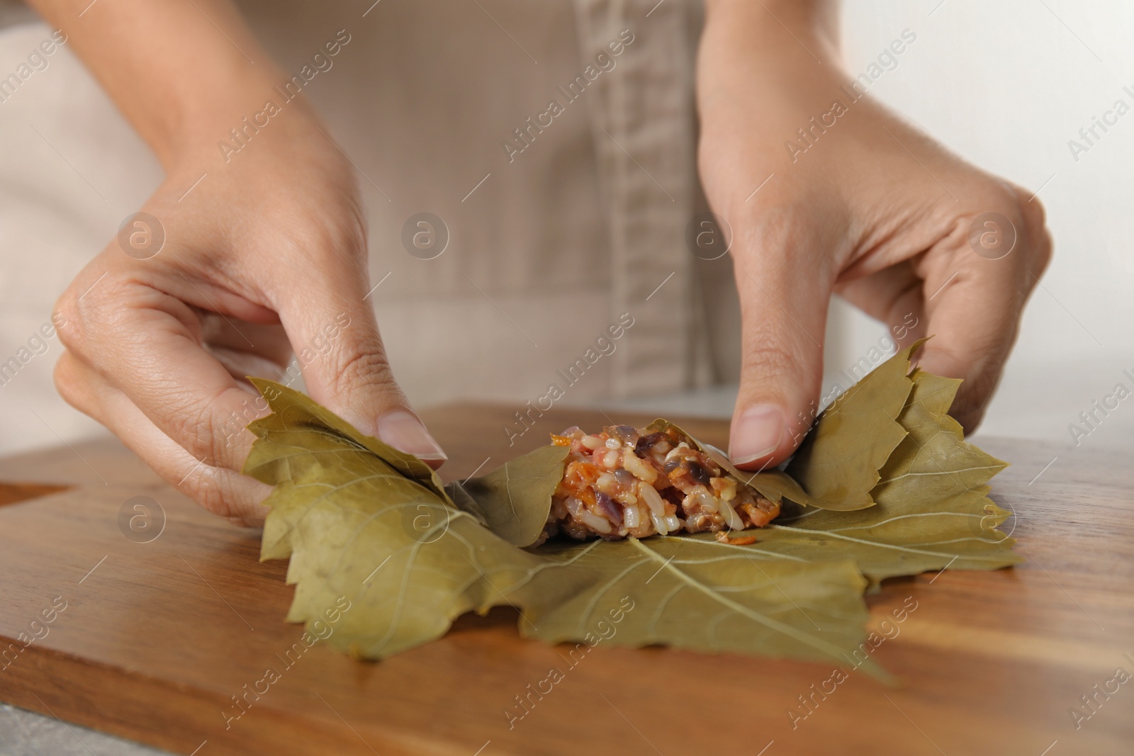 Photo of Woman preparing stuffed grape leaves on wooden board, closeup