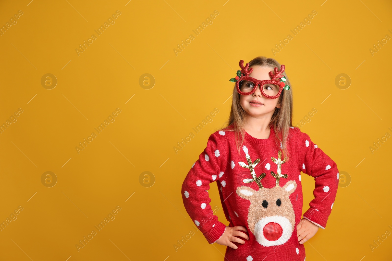 Photo of Cute little girl in Christmas sweater and party glasses on yellow background, space for text