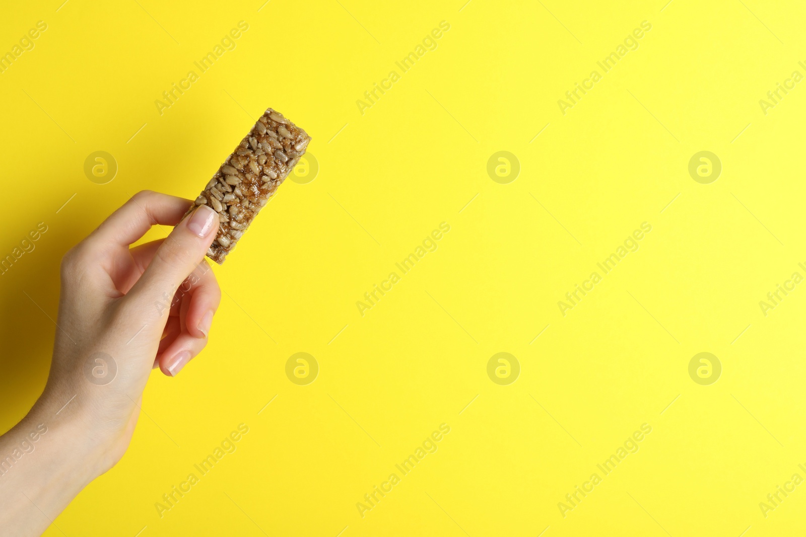 Photo of Woman holding kozinaki bar on yellow background, closeup. Space for text