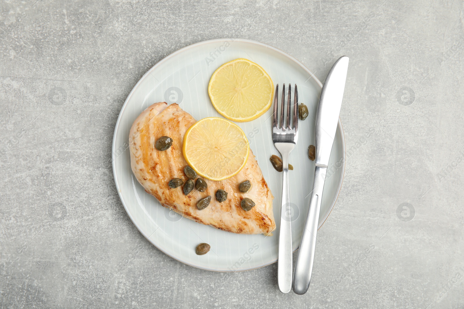 Photo of Delicious chicken fillet with capers and lemon served on light grey table, top view