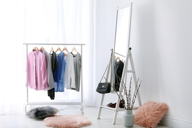 Photo of Rack with clothes and modern mirror in light room