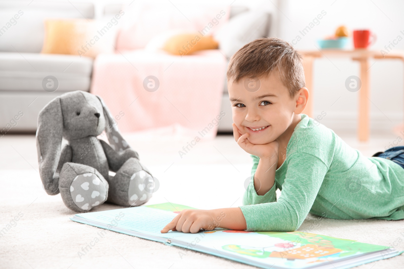 Photo of Little boy with toy reading book on floor at home