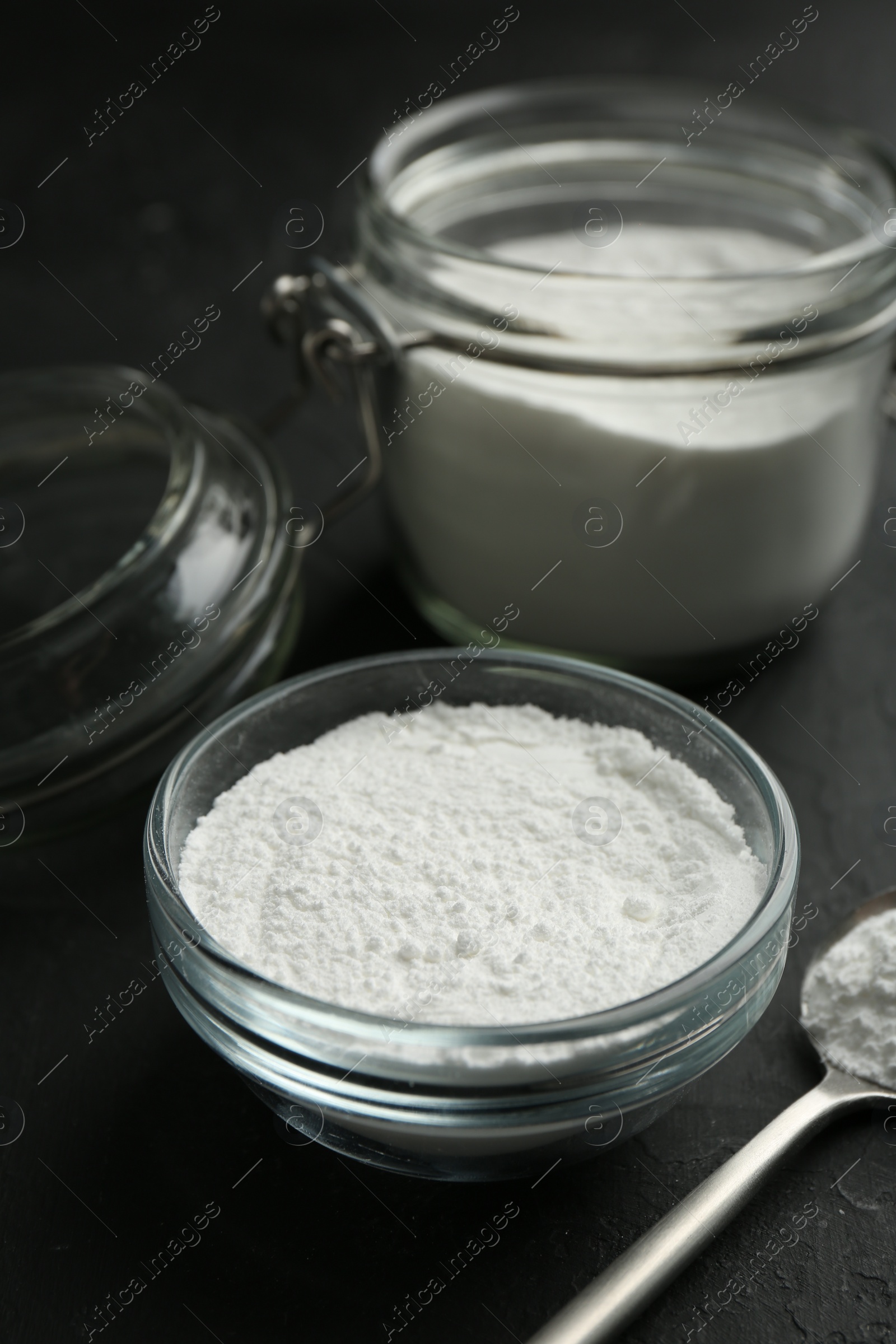 Photo of Baking powder in bowl, jar and spoon on black textured table, closeup