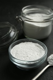 Photo of Baking powder in bowl, jar and spoon on black textured table, closeup