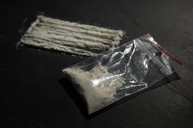 Photo of Drug addiction. Plastic bag with cocaine on dark textured table, closeup