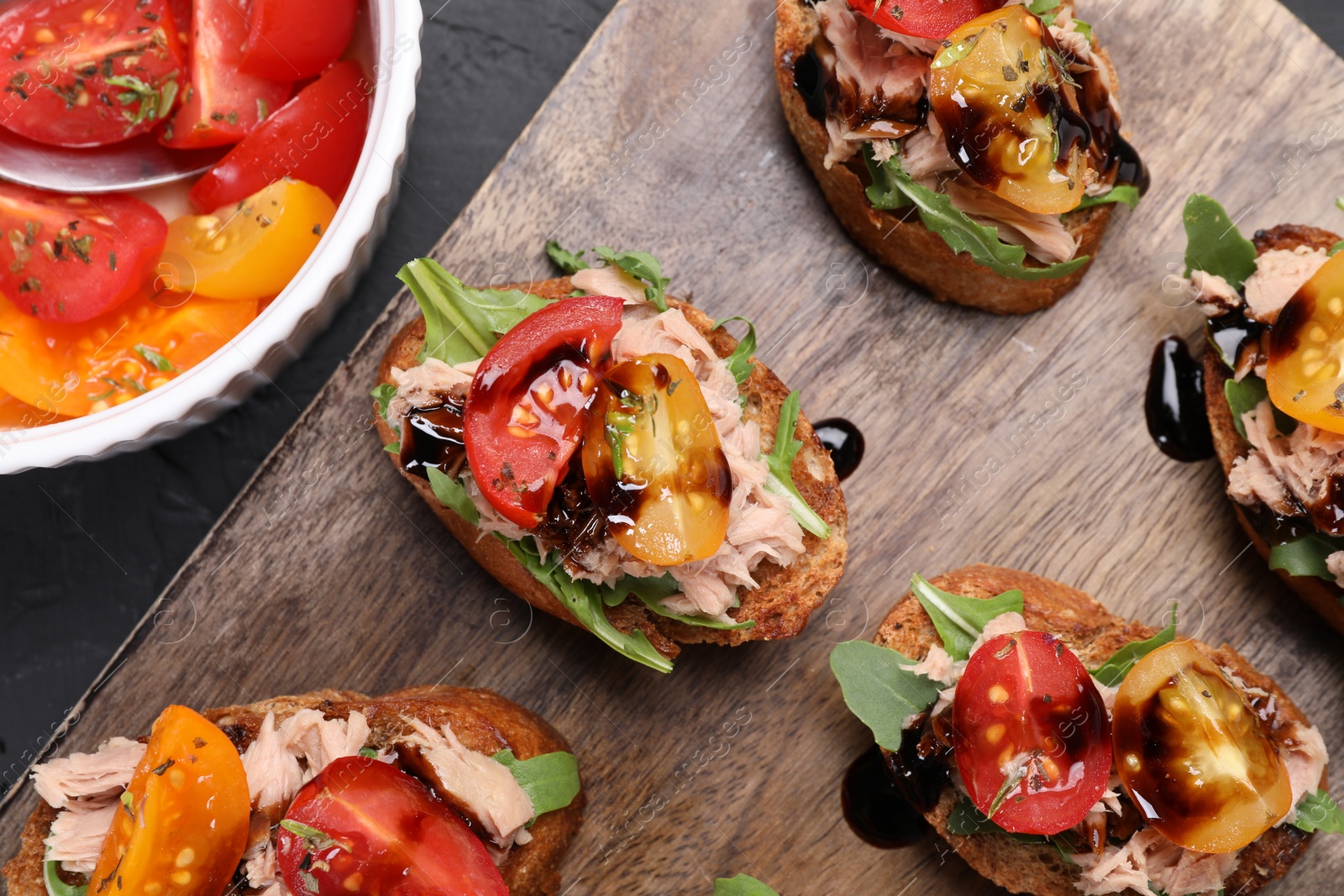 Photo of Delicious bruschettas with balsamic vinegar, tomatoes, arugula and tuna on dark textured table, flat lay