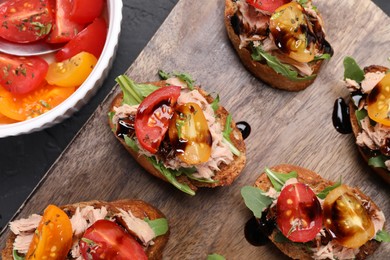 Photo of Delicious bruschettas with balsamic vinegar, tomatoes, arugula and tuna on dark textured table, flat lay