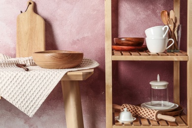 Photo of Wooden shelving unit and table with kitchenware near color wall