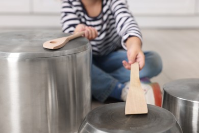 Photo of Little girl pretending to play drums on pots indoors, closeup