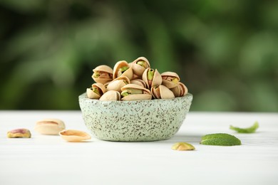 Tasty pistachios in bowl on white table against blurred background