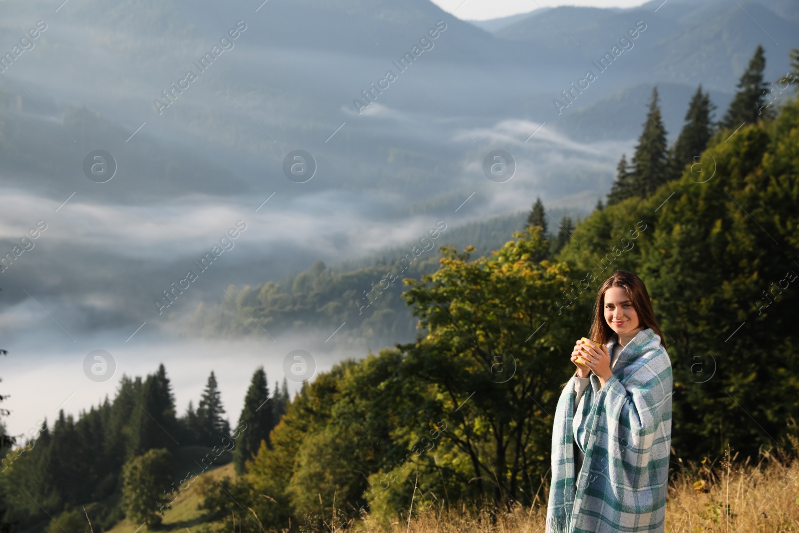 Photo of Young woman with cup of hot drink and plaid enjoying beautiful mountain landscape. Space for text