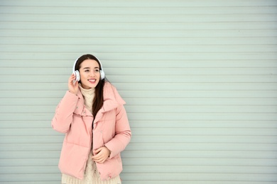 Photo of Beautiful young woman listening to music with headphones against light wall. Space for text