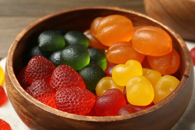 Photo of Delicious gummy candies in wooden bowl, closeup