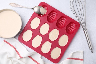 Photo of Baking mold for madeleine cookies with batter and spoon on white table, flat lay