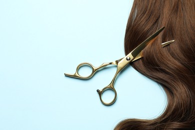 Professional hairdresser scissors with brown hair strand on light blue background, top view. Space for text