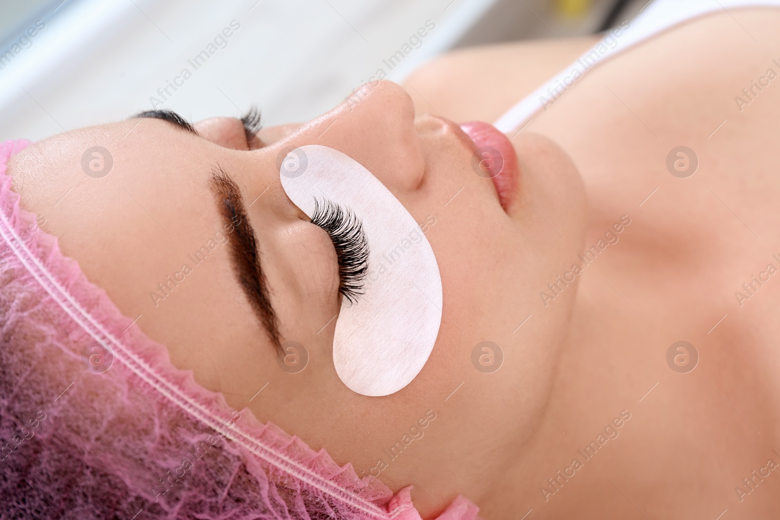 Photo of Young woman undergoing eyelash extensions procedure, closeup