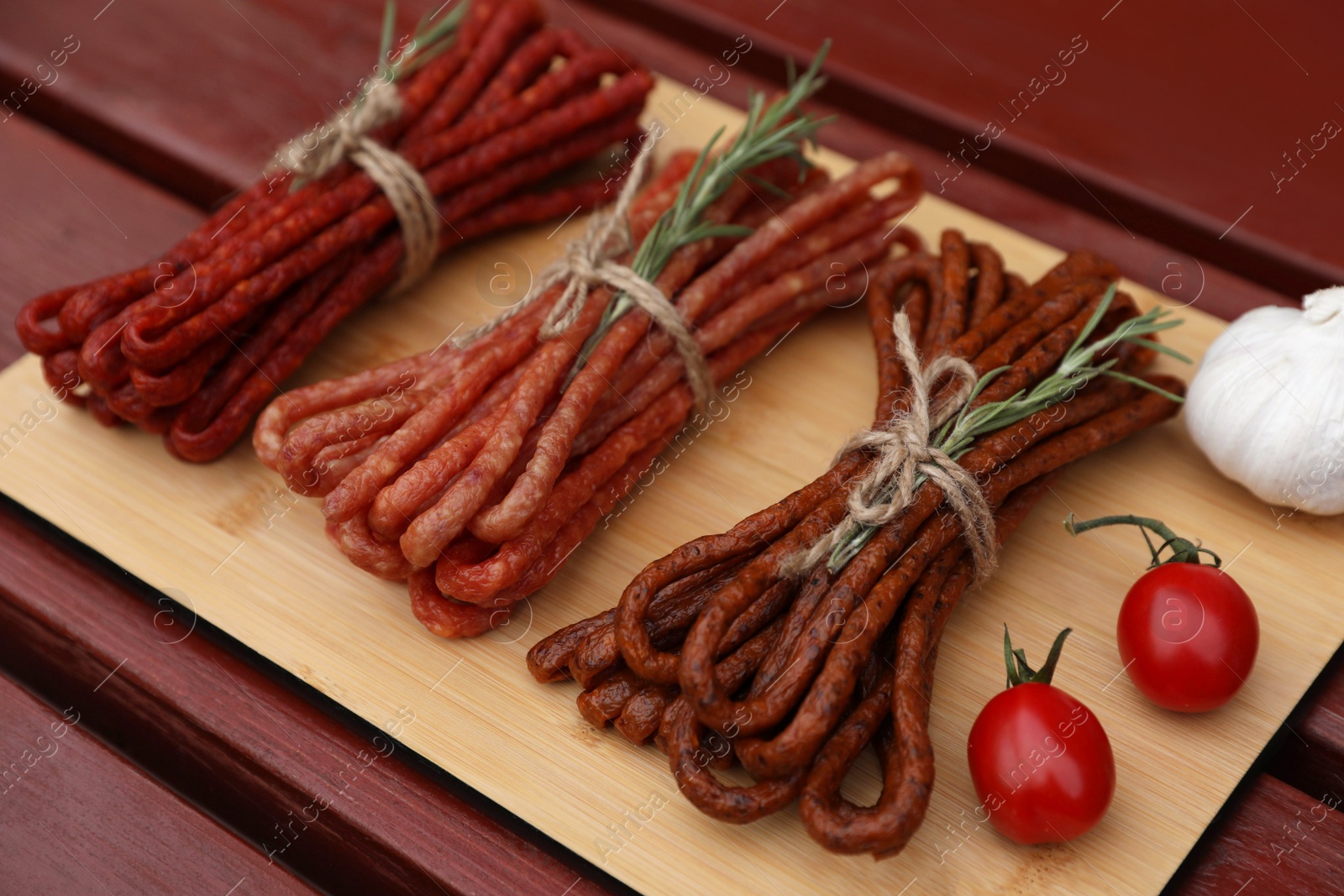 Photo of Bundles of delicious kabanosy with rosemary, tomatoes and garlic on wooden table