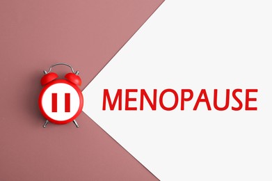 Menopause word and alarm clock with pause symbol on color background, top view