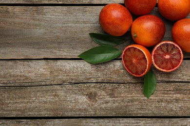 Many ripe sicilian oranges and leaves on wooden table, flat lay. Space for text