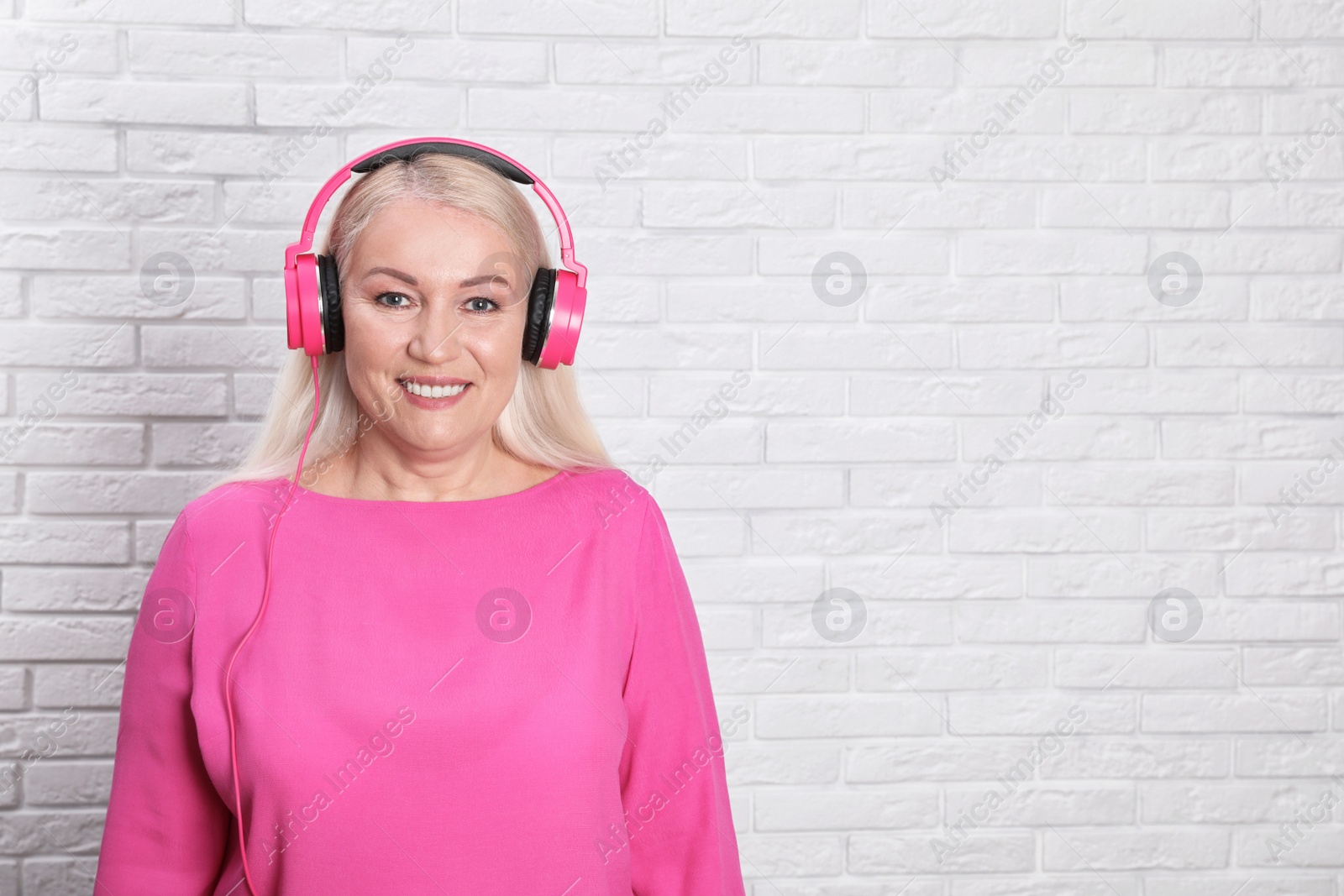 Photo of Mature woman enjoying music in headphones against brick wall. Space for text