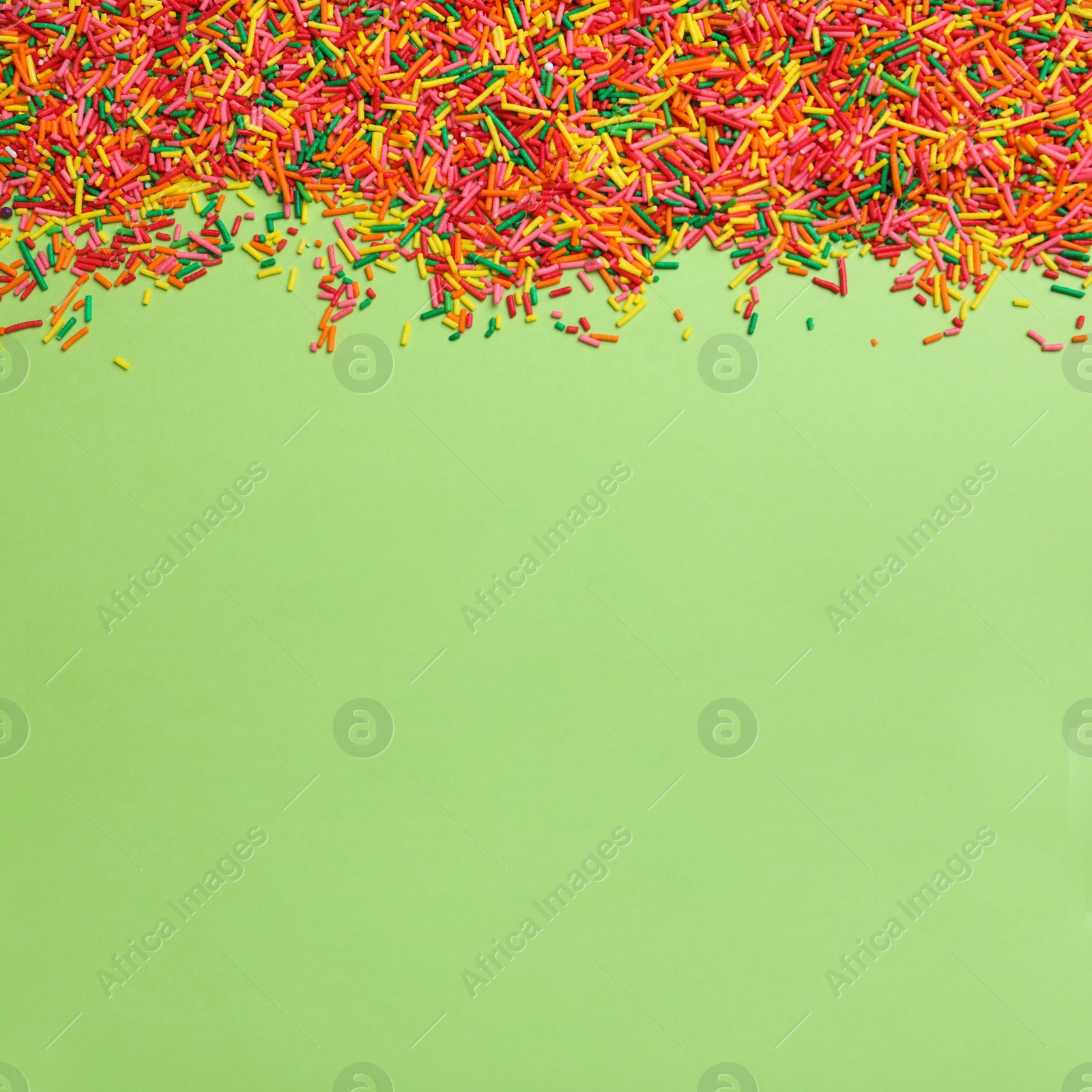 Photo of Colorful sprinkles on green background, flat lay with space for text. Confectionery decor